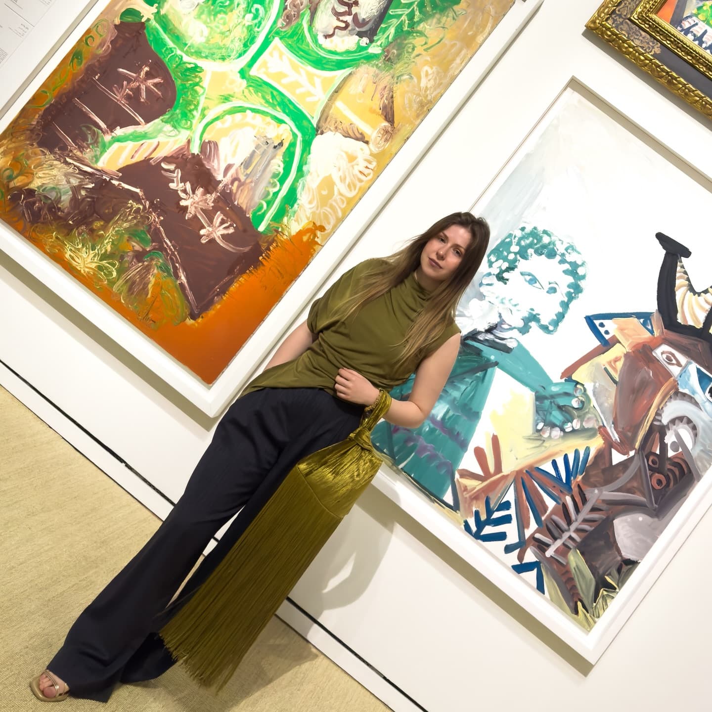 Daryna leaning against a gallery wall between two paintings