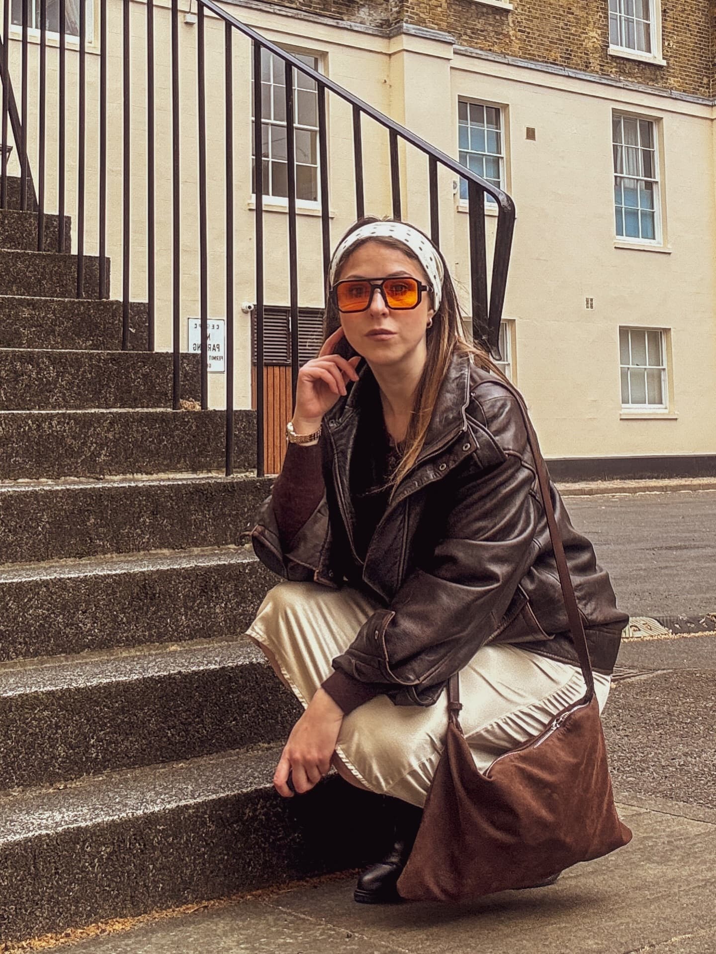 Daryna crouched on London steps in a leather jacket and satin trousers